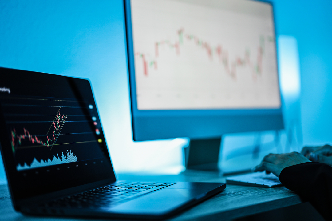 laptop and monitor displaying upward trending graphs